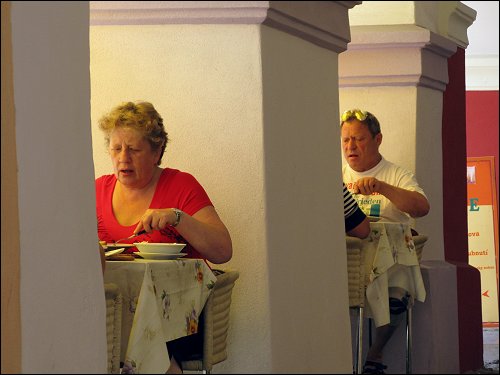 speisende Restaurantgäste zwischen Straße (links) und Arkadengang (rechts)