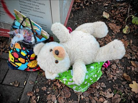 Hilfeheischender Teddy am überfüllten Altkleider-Container